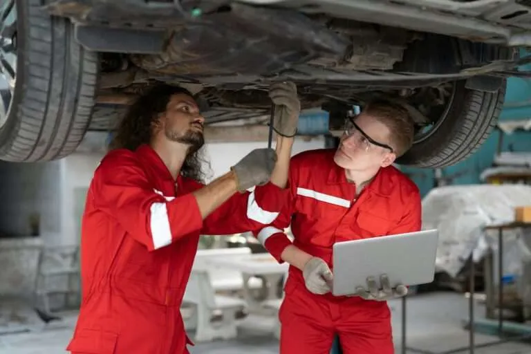 Two technicians inspecting a vehicle's axle and underbody on a lift