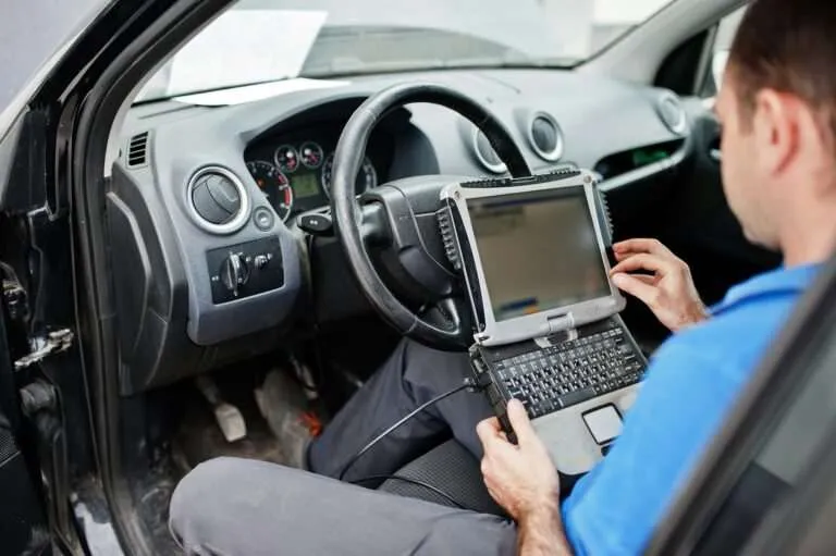 Technician reading vehicle data on a laptop scan tool from the driver's seat