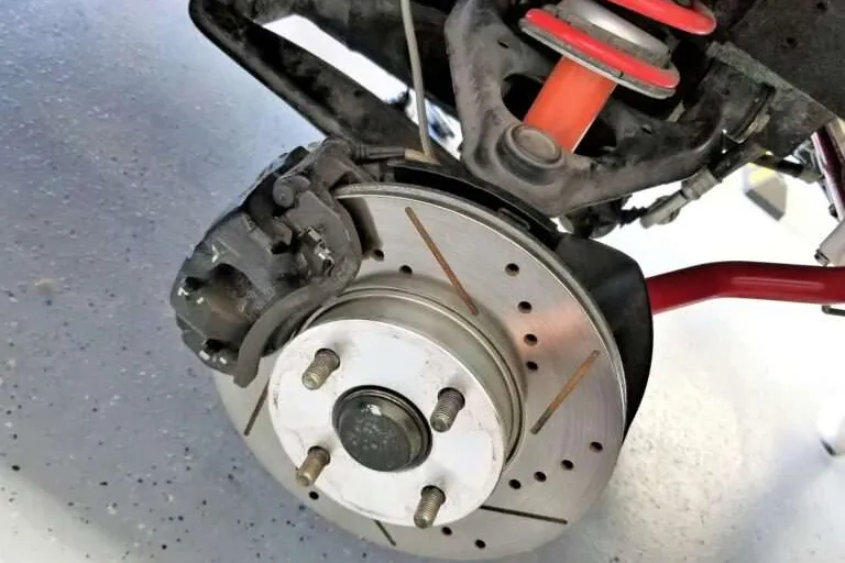 Front strut assembly with coil spring above a drilled brake rotor