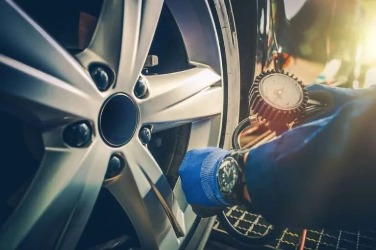 Technician checking tire pressure with a gauge on an alloy wheel